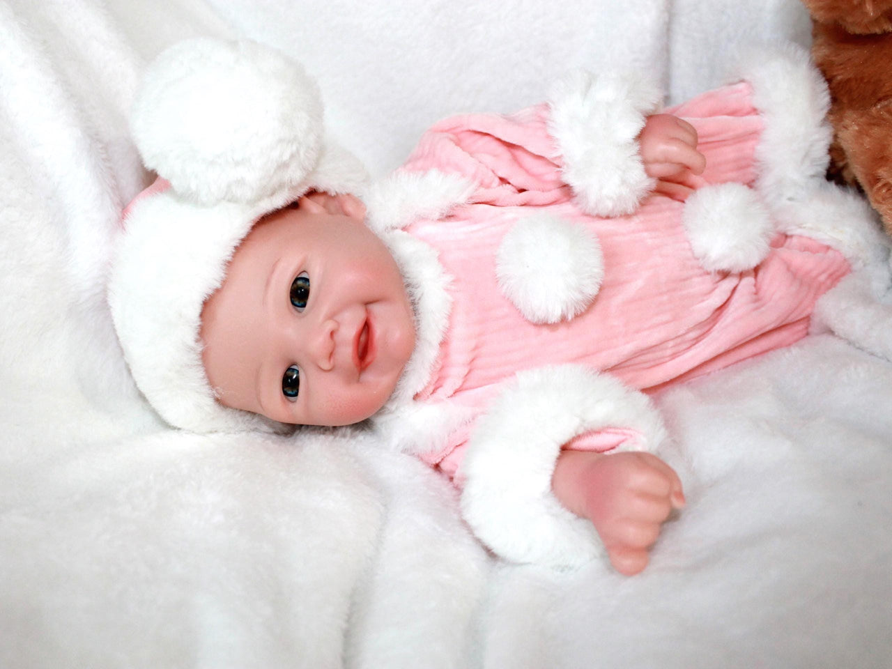 A baby doll wearing a pink and white outfit, featuring a sweet expression and soft, cuddly features.