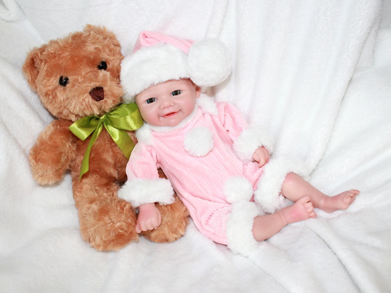 A baby doll dressed in pink, cradling a teddy bear, is positioned on a cozy surface.