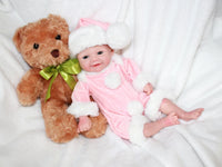 Thumbnail for A baby doll dressed in pink, cradling a teddy bear, is positioned on a cozy surface.