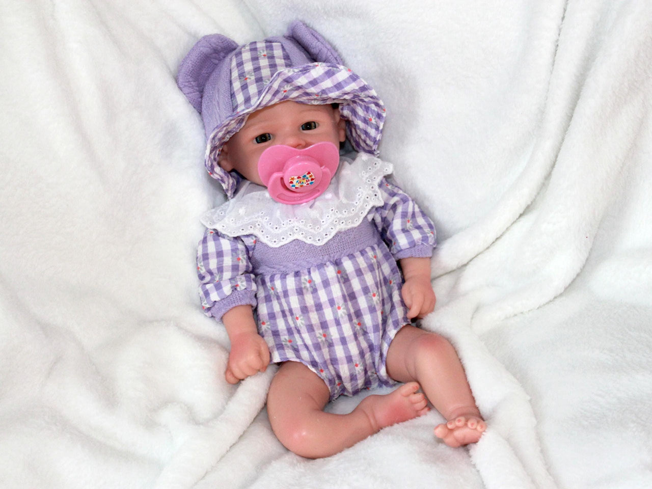 A baby doll wearing a charming purple and white dress, showcasing delicate details and a friendly smile.