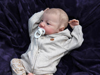 Thumbnail for A baby doll resting on a soft blanket, showcasing its delicate features and clothing.