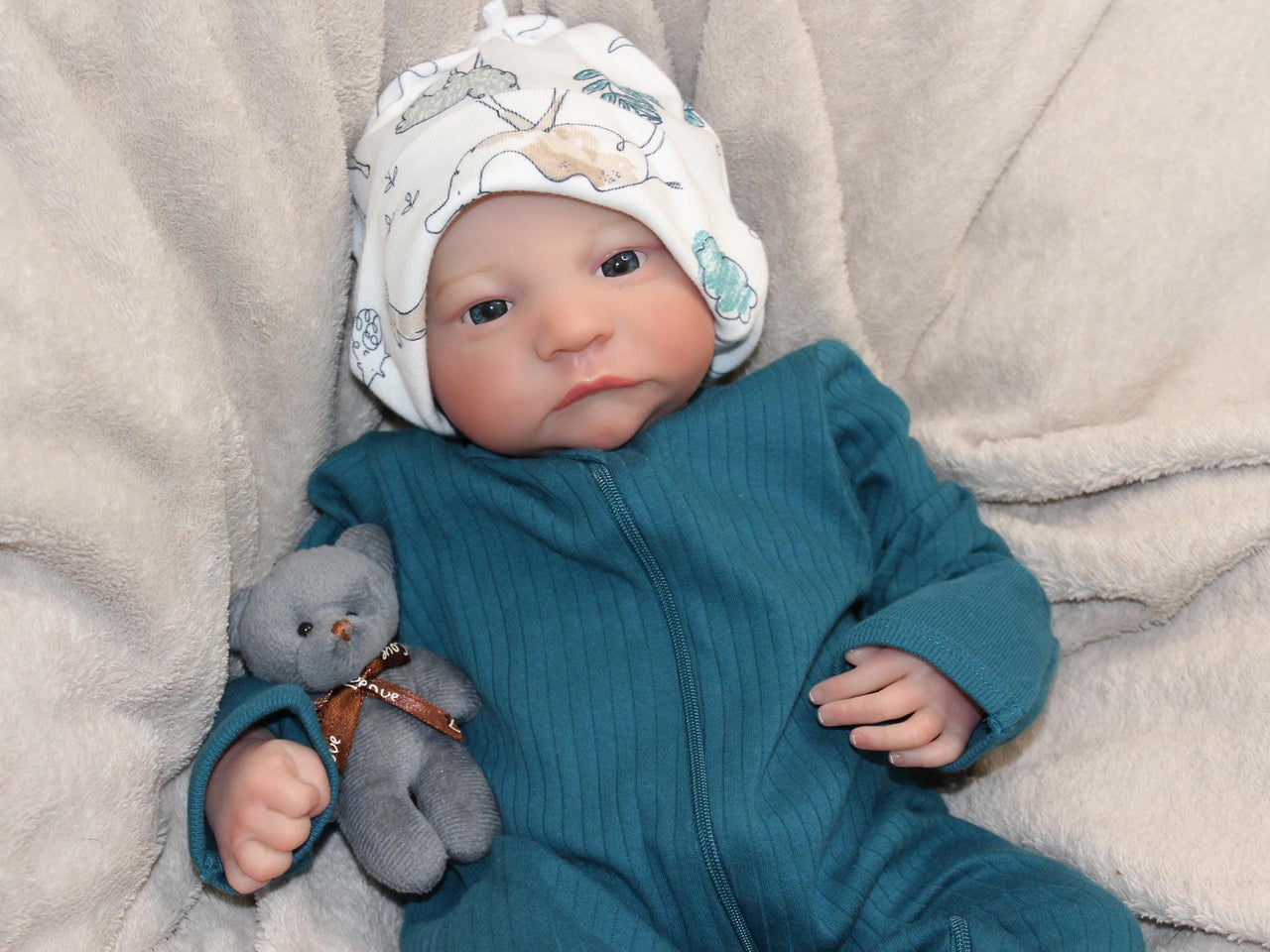 A baby doll rests on a soft blanket beside a cuddly teddy bear, creating a cozy and playful scene.