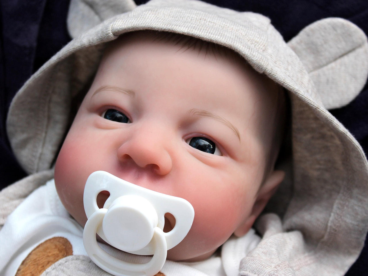 An infant wearing a hat, comfortably resting on a colorful blanket, exuding a sense of tranquilit