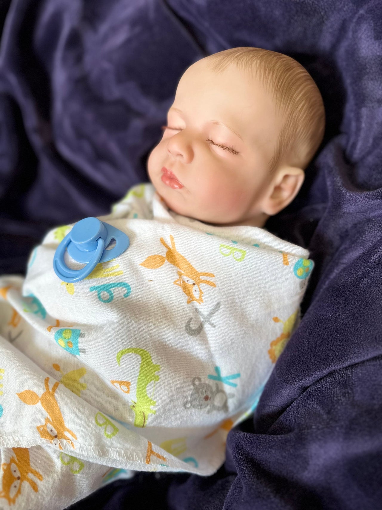 Sleeping reborn baby doll swaddled in animal print blanket with blue pacifier, lifelike handmade newborn doll for collectors or therapy