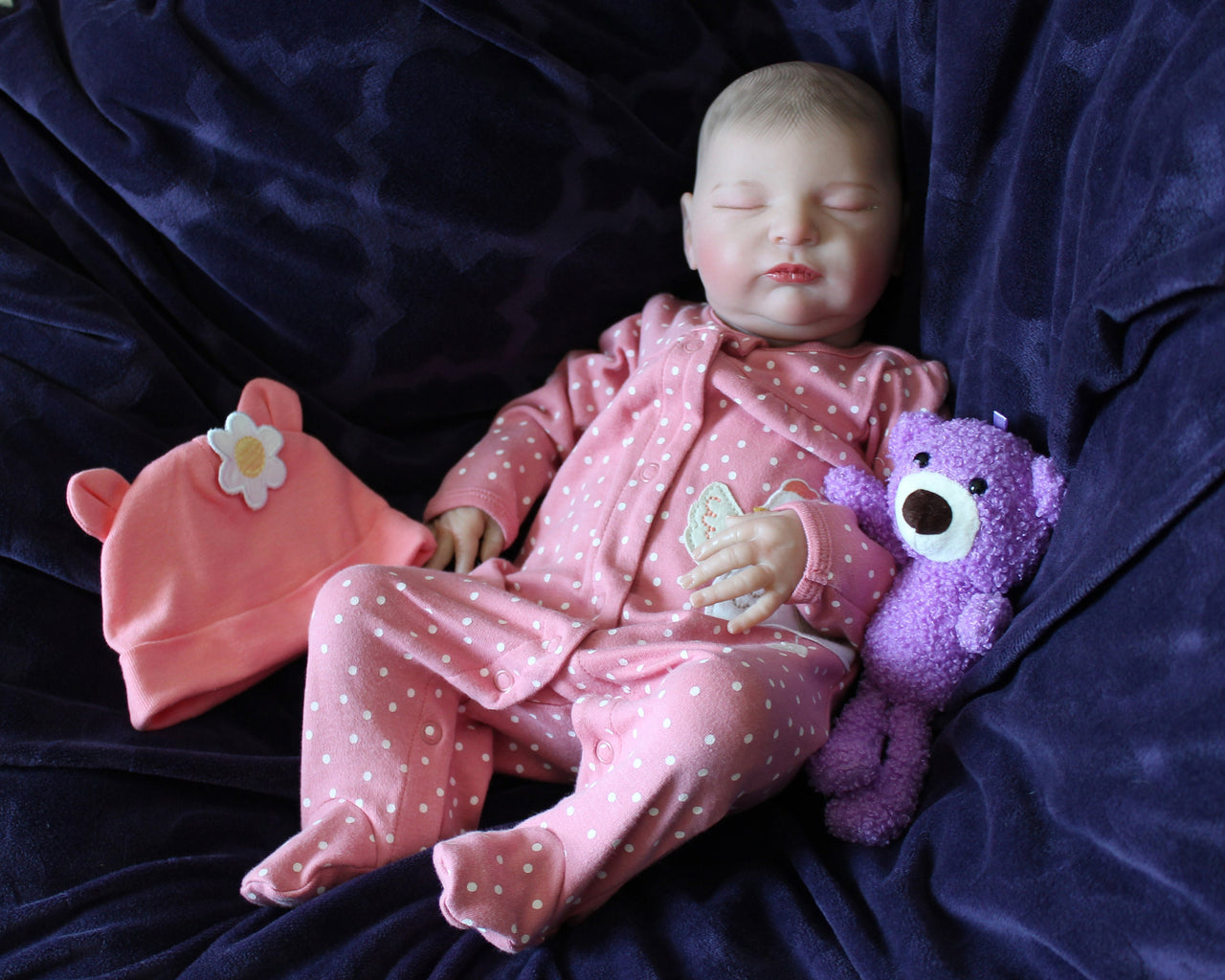 A baby doll positioned on a vibrant purple blanket, highlighting its charming expression and colorful outfit.