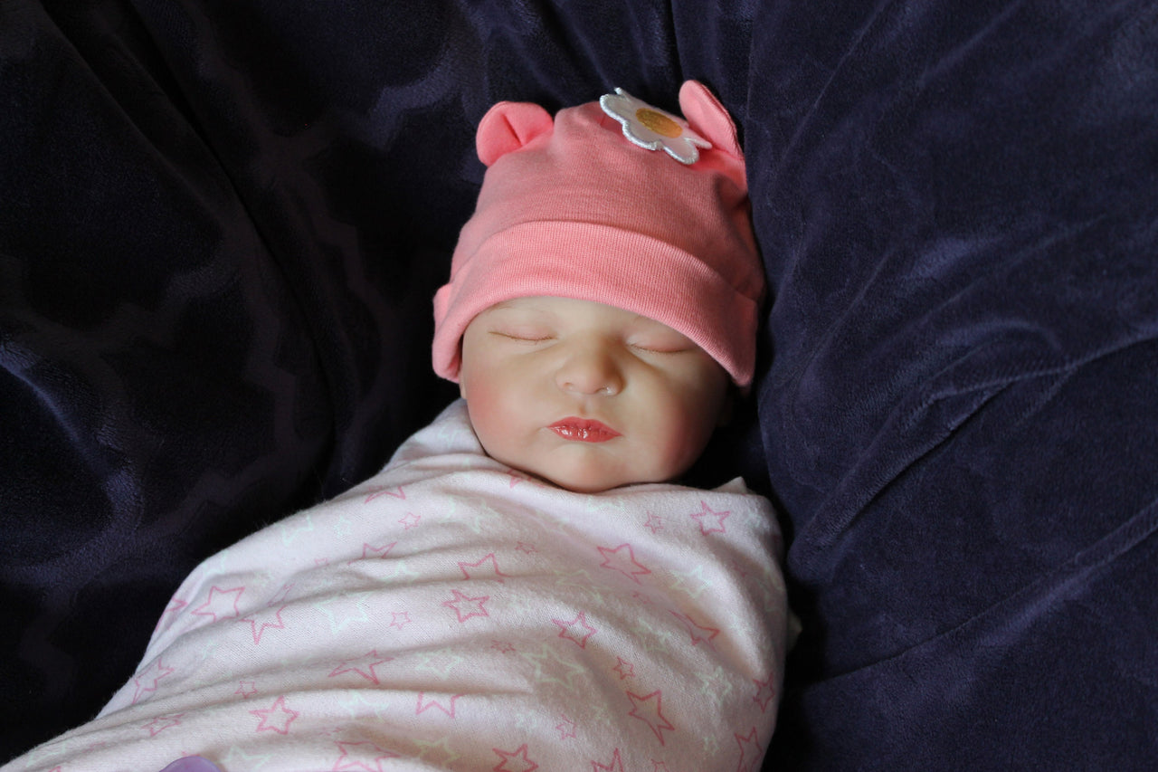 A baby doll lying on a cozy purple blanket, emphasizing its sweet face and playful attire.