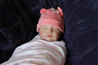Thumbnail for A baby doll lying on a cozy purple blanket, emphasizing its sweet face and playful attire.