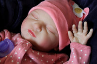 Thumbnail for A baby doll resting on a soft purple blanket, showcasing its delicate features and bright clothing.