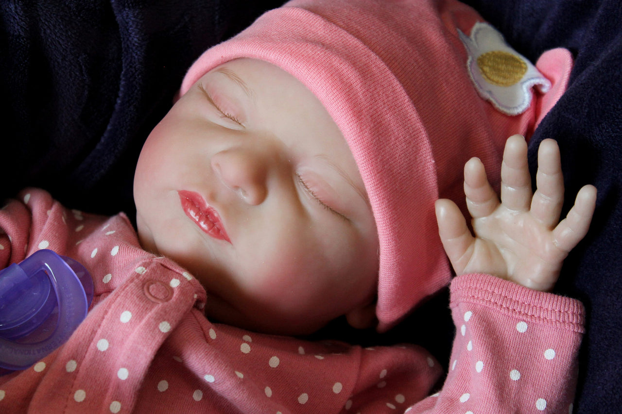 A baby doll resting on a soft purple blanket, showcasing its delicate features and bright clothing.