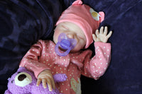 Thumbnail for A baby doll positioned on a vibrant purple blanket, highlighting its charming expression and colorful outfit.