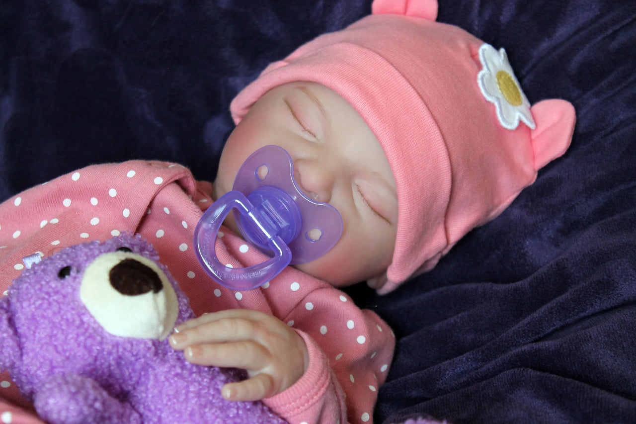 A baby doll positioned on a vibrant purple blanket, highlighting its charming expression and colorful outfit.