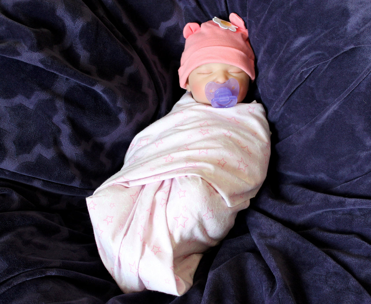 A baby doll positioned on a vibrant purple blanket, highlighting its charming expression and colorful outfit.