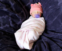 Thumbnail for A baby doll positioned on a vibrant purple blanket, highlighting its charming expression and colorful outfit.