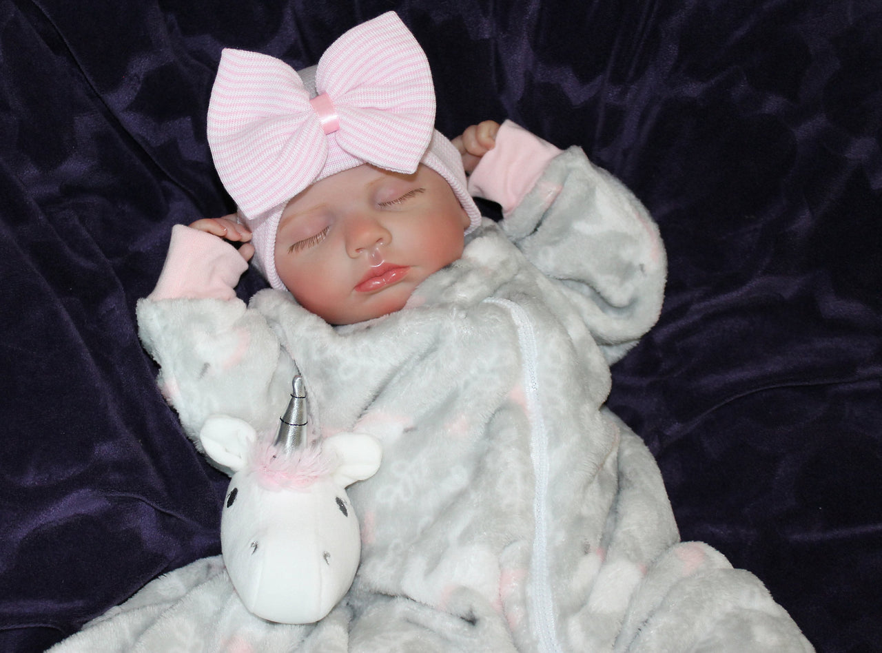A newborn baby girl dressed in gray with a pink bow, sleeping adorably on a cozy surface.