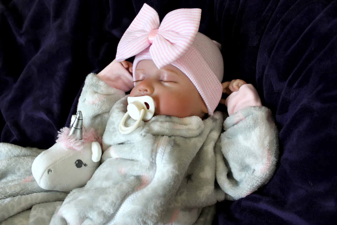 A newborn baby girl dressed in gray with a pink bow, sleeping adorably on a cozy surface.