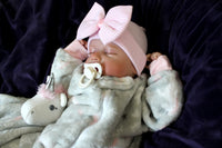 Thumbnail for A newborn baby girl dressed in gray with a pink bow, sleeping adorably on a cozy surface.