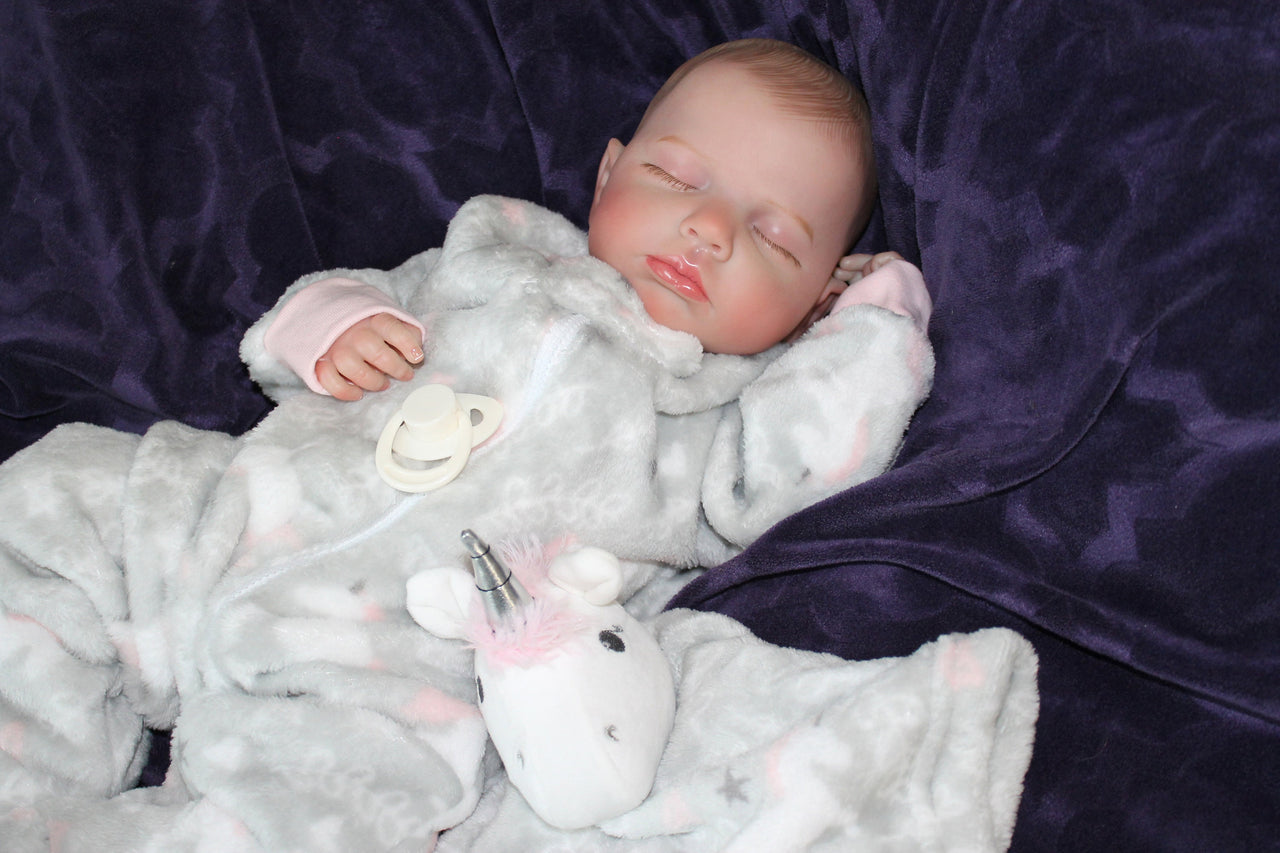 Newborn baby girl in a gray outfit with a pink bow, peacefully resting on a soft blanket.