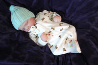 Thumbnail for A baby in a hat and onesie lies on a soft purple blanket, looking peaceful and content.