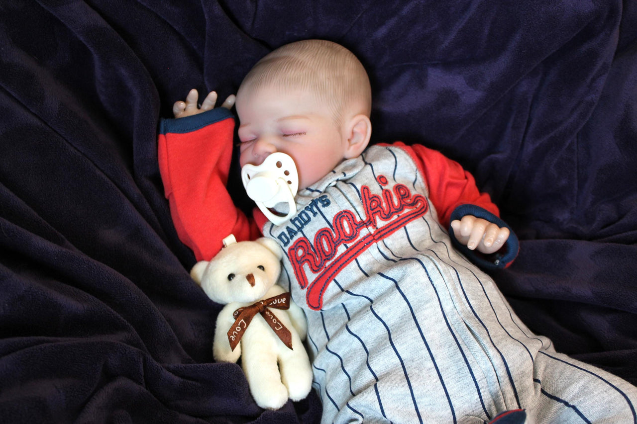 A baby wearing a baseball outfit rests on a cozy purple blanket, showcasing a delightful and playful appearance.