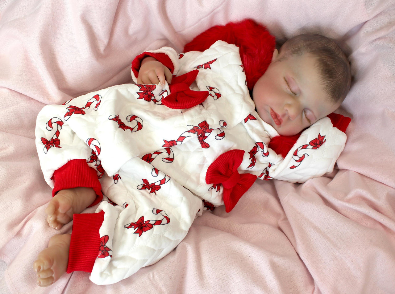 reborn doll in a red and white candy cane outfit with a furry red hood