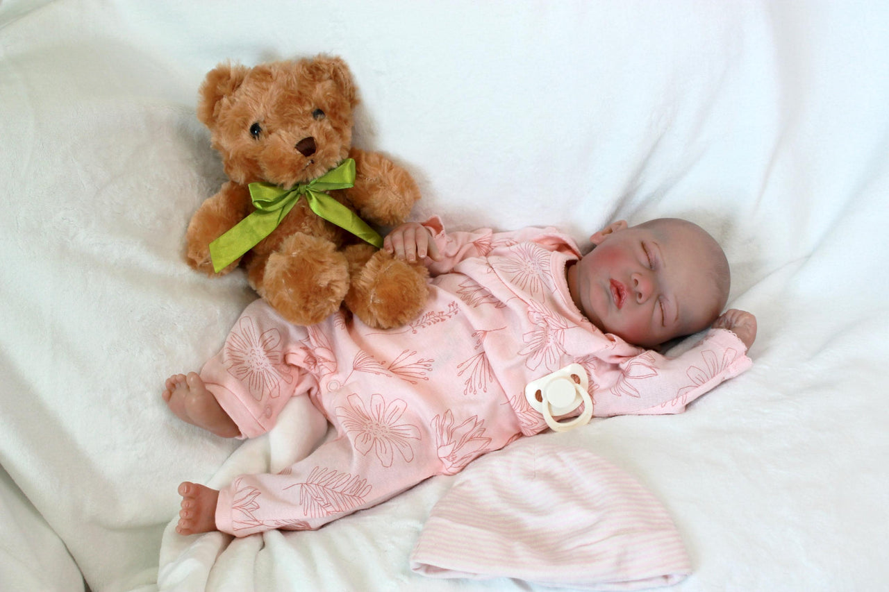 A baby doll peacefully sleeps, dressed in a soft pink outfit, exuding a sense of calm and innocence.