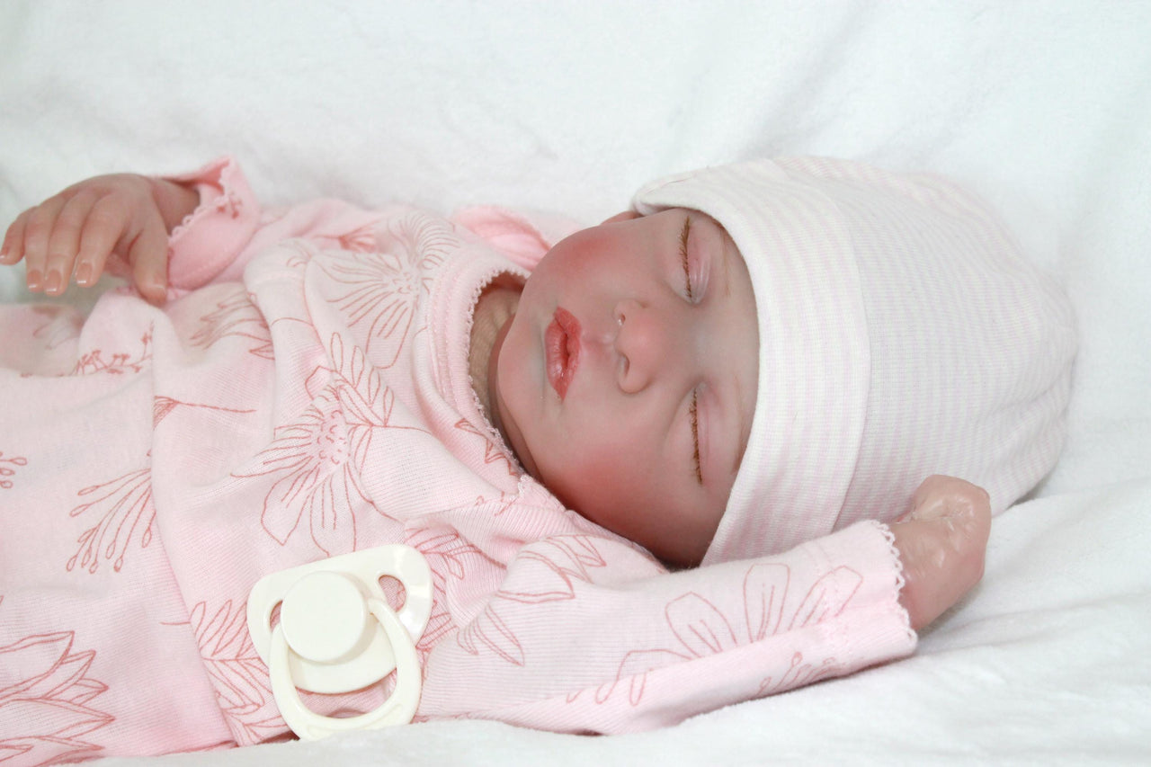 A serene baby doll in a pink outfit is sleeping, embodying tranquility and charm in its delicate appearance.