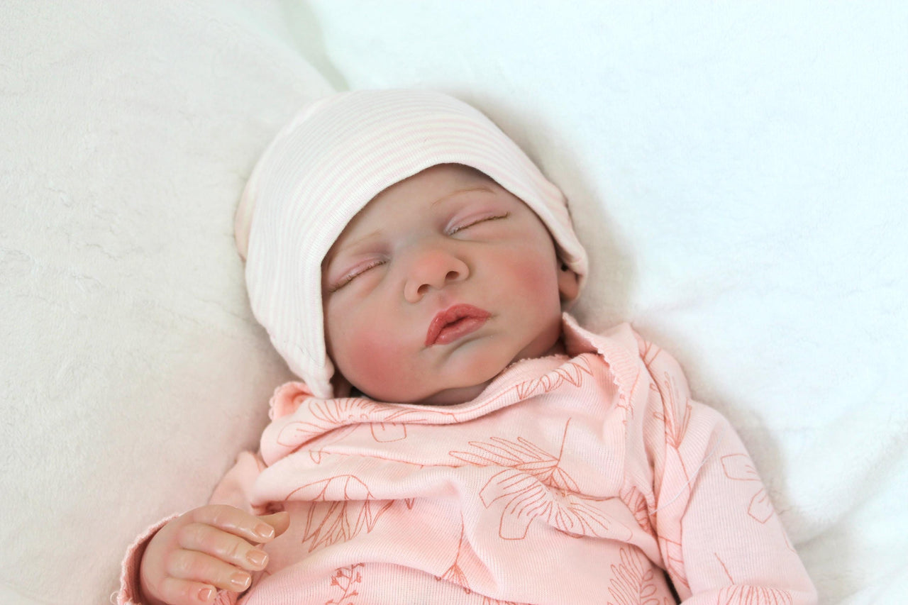 A serene baby doll in a pink outfit is sleeping, embodying tranquility and charm in its delicate appearance.