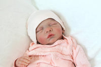 Thumbnail for A serene baby doll in a pink outfit is sleeping, embodying tranquility and charm in its delicate appearance.