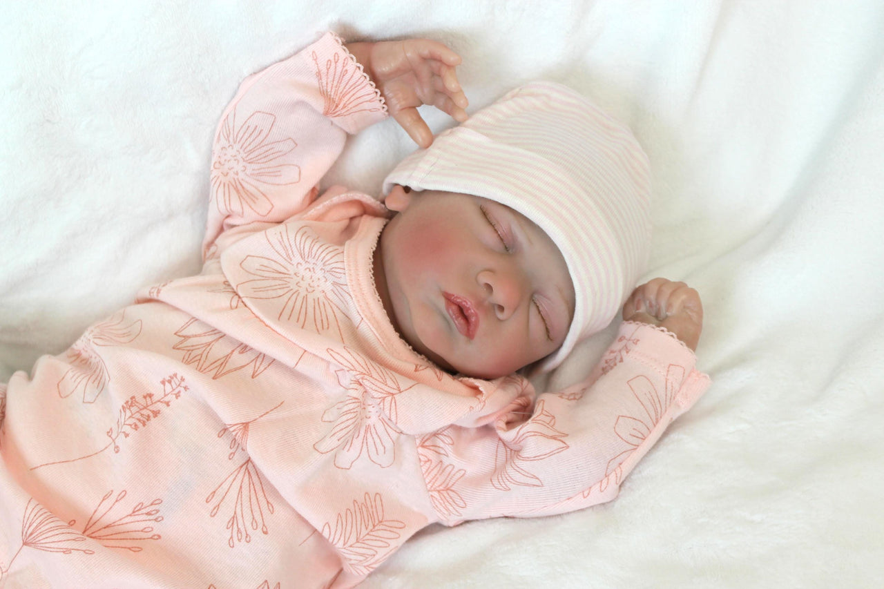 A baby doll, adorned in a pink outfit, is soundly sleeping, radiating a gentle and soothing presence.