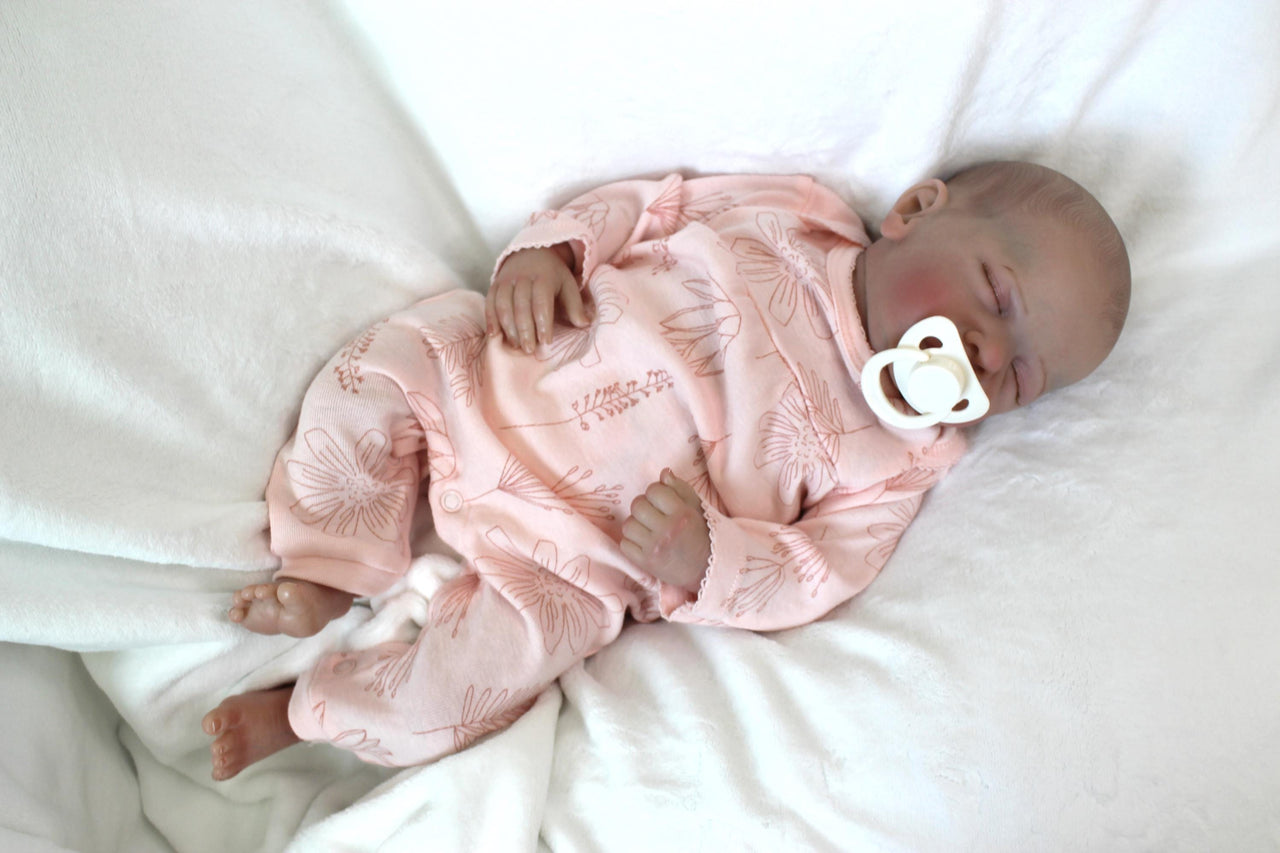 A baby doll peacefully sleeps, dressed in a soft pink outfit, exuding a sense of calm and innocence.