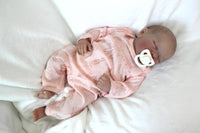 Thumbnail for A baby doll peacefully sleeps, dressed in a soft pink outfit, exuding a sense of calm and innocence.