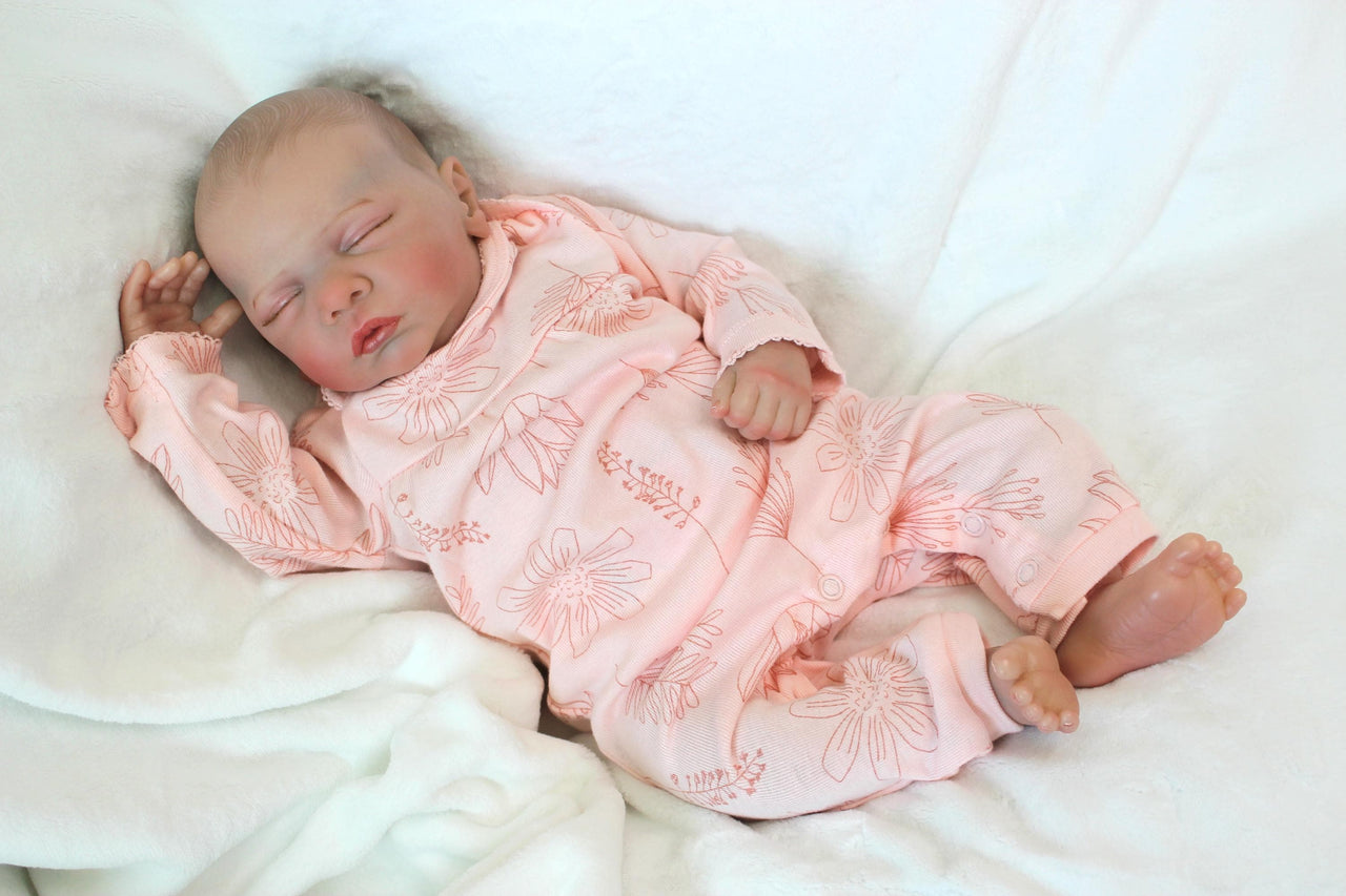 A baby doll peacefully sleeps, dressed in a soft pink outfit, exuding a sense of calm and innocence.