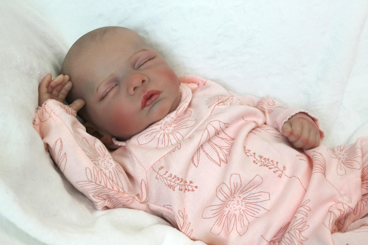 A baby doll peacefully sleeps, dressed in a soft pink outfit, exuding a sense of calm and innocence.