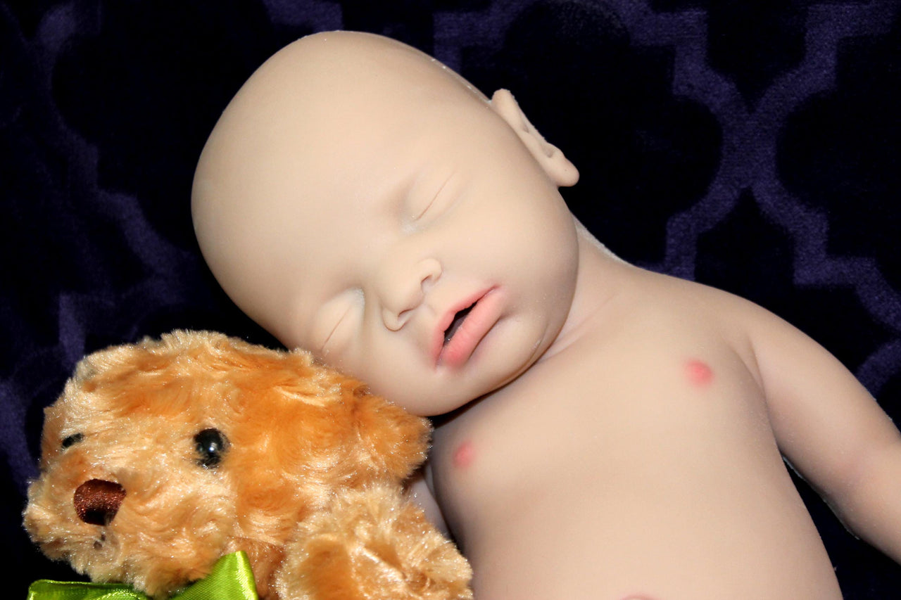 Full Silicone Doll baby doll lies on a vibrant purple blanket, accompanied by a charming teddy bear, evoking a sense of comfort and joy.