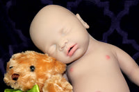 Thumbnail for Full Silicone Doll baby doll lies on a vibrant purple blanket, accompanied by a charming teddy bear, evoking a sense of comfort and joy.