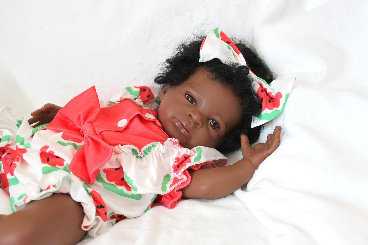 A black baby doll resting peacefully on a white bed, showcasing its soft features and delicate attire.
