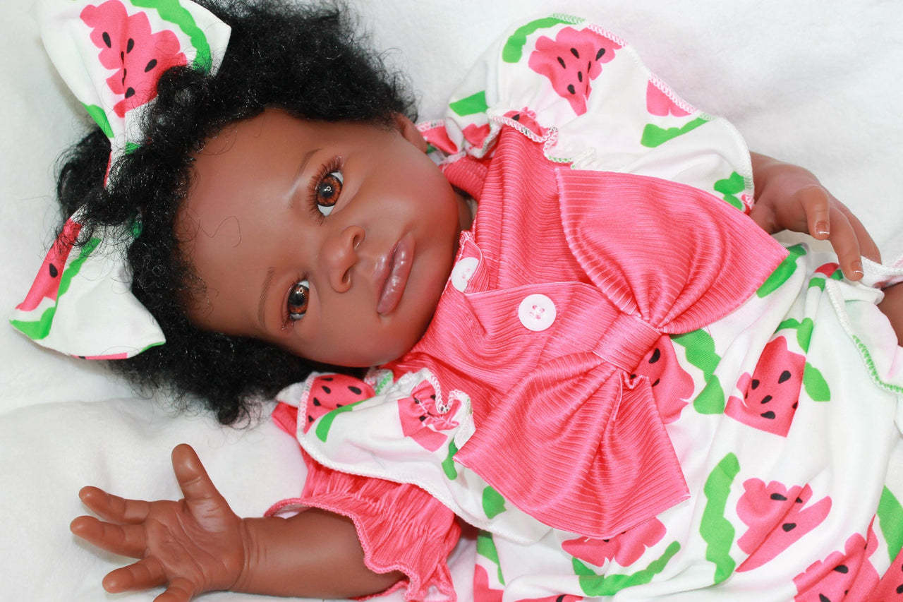 A black baby doll lying on a white bed, emphasizing its adorable appearance in a serene and simple setting.
