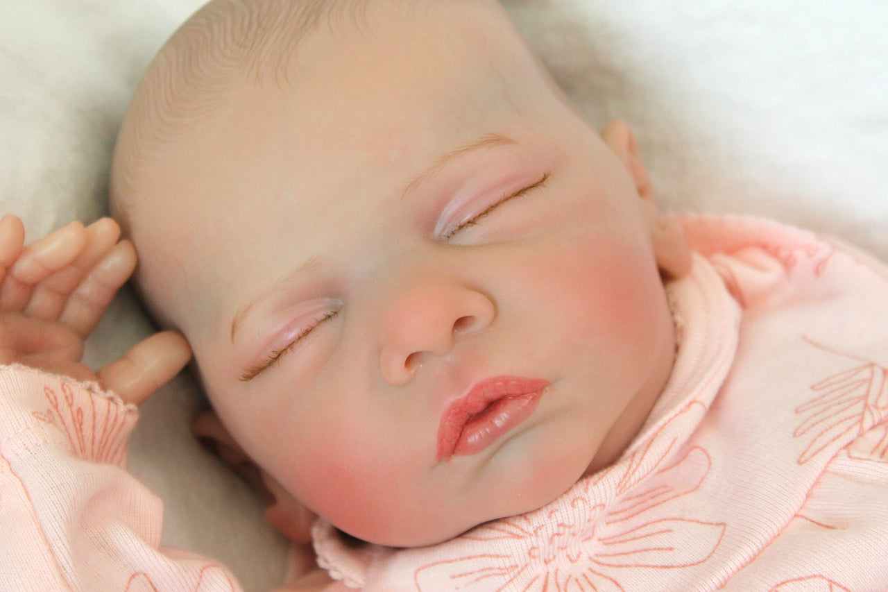 A serene baby doll in a pink outfit is sleeping, embodying tranquility and charm in its delicate appearance.