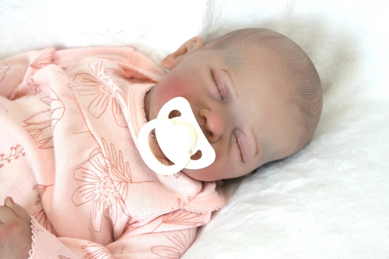 A baby doll, adorned in a pink outfit, is soundly sleeping, radiating a gentle and soothing presence.