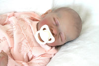 Thumbnail for A baby doll, adorned in a pink outfit, is soundly sleeping, radiating a gentle and soothing presence.