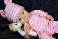 Thumbnail for A baby doll dressed in a pink and white striped outfit, sitting upright with a cheerful expression.