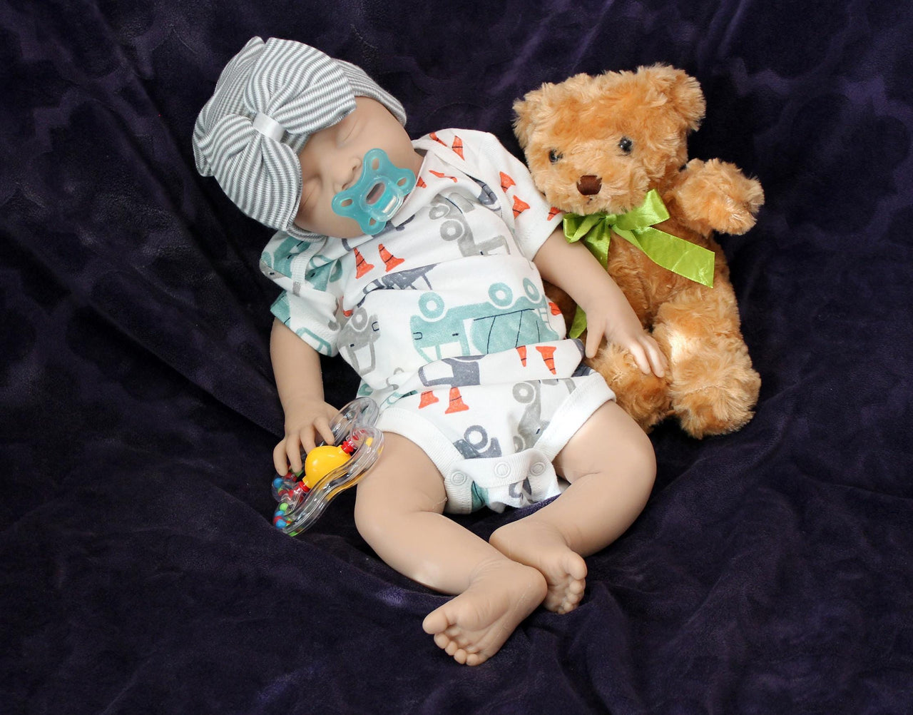 Full Silicone Doll baby doll lies on a vibrant purple blanket, accompanied by a charming teddy bear, evoking a sense of comfort and joy.