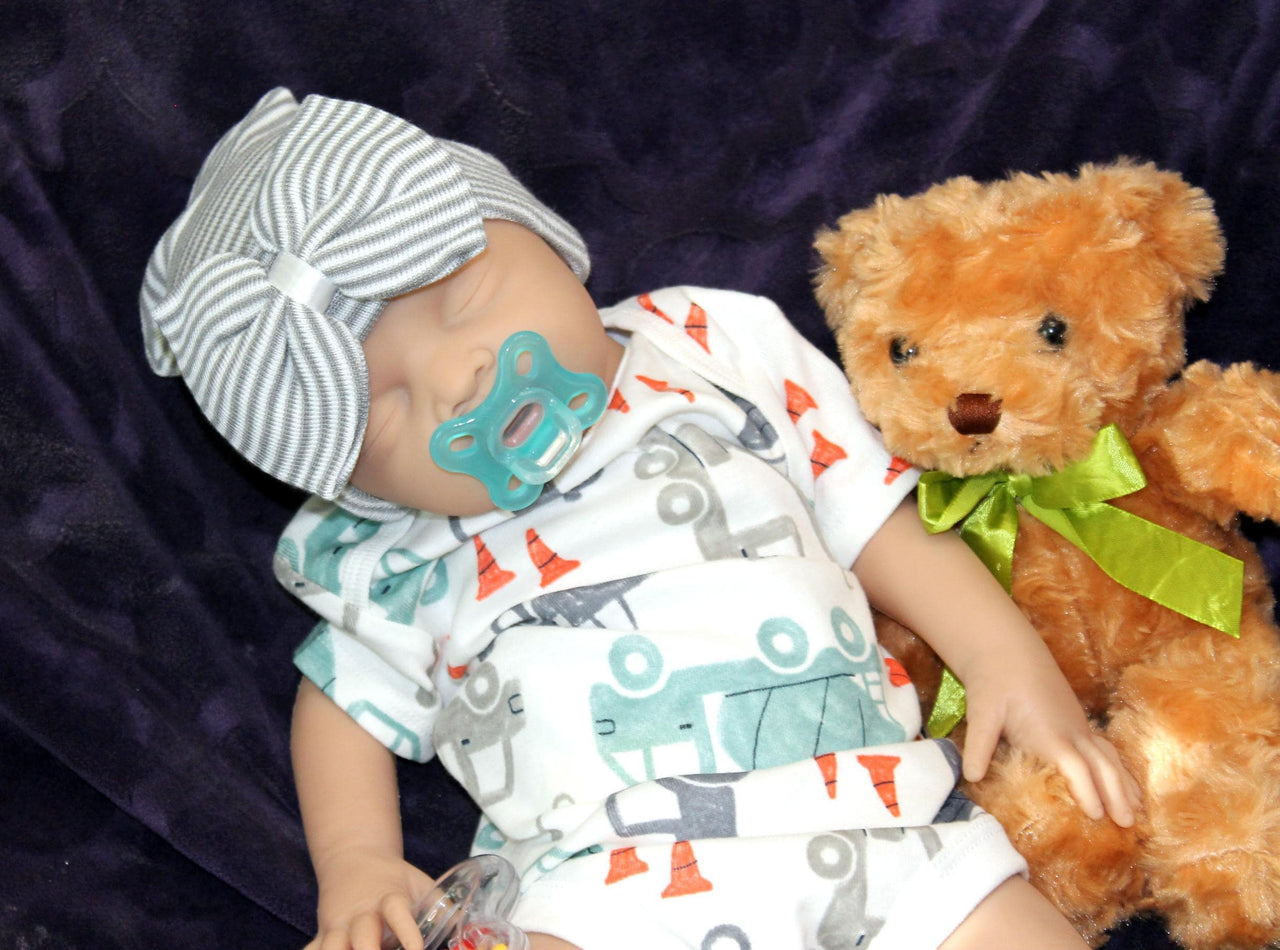 Full Silicone Doll baby doll rests on a soft purple blanket beside a cuddly teddy bear, creating a serene and playful scene.