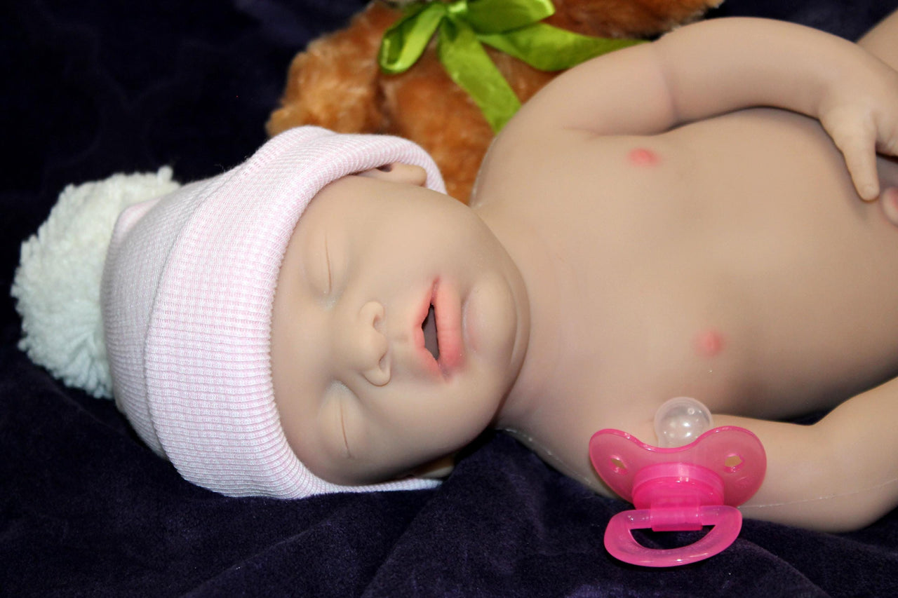 Full Silicone Doll baby doll is positioned on a purple blanket, next to a teddy bear, illustrating a delightful and cozy atmosphere.