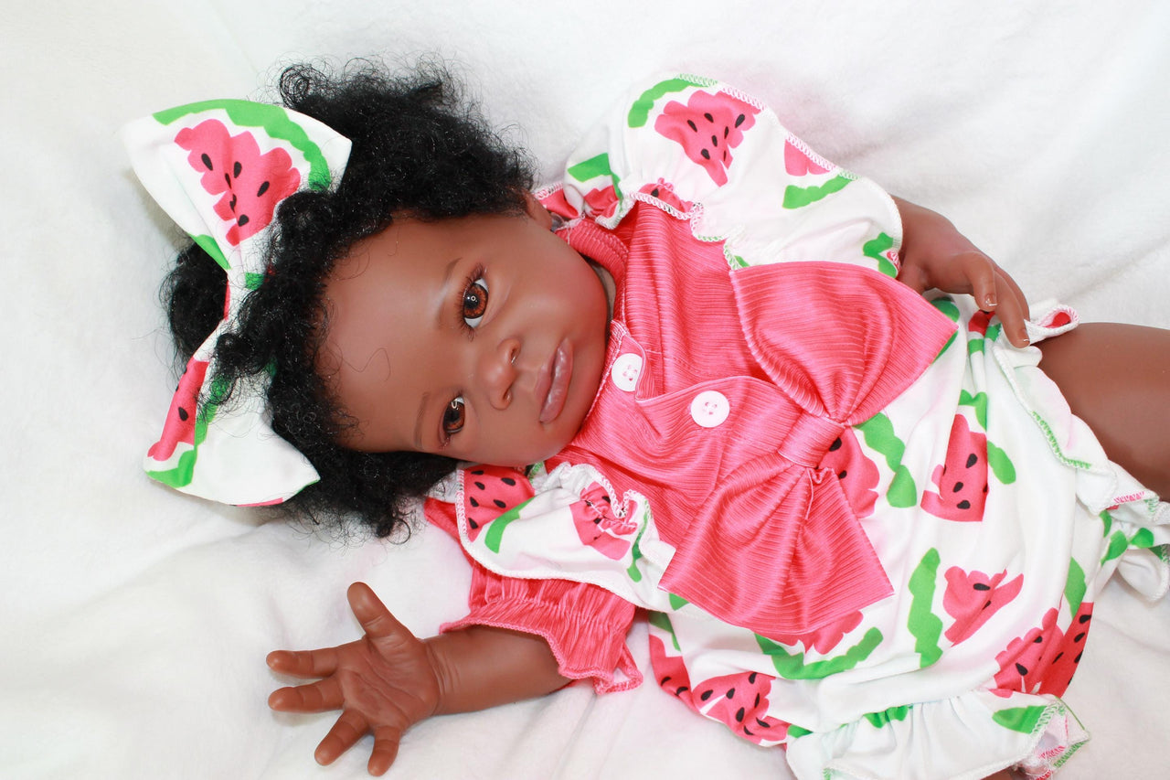 A black baby doll resting peacefully on a white bed, showcasing its soft features and delicate attire.