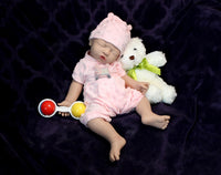Thumbnail for A baby doll sits beside a teddy bear and a colorful toy, creating a charming and playful scene.