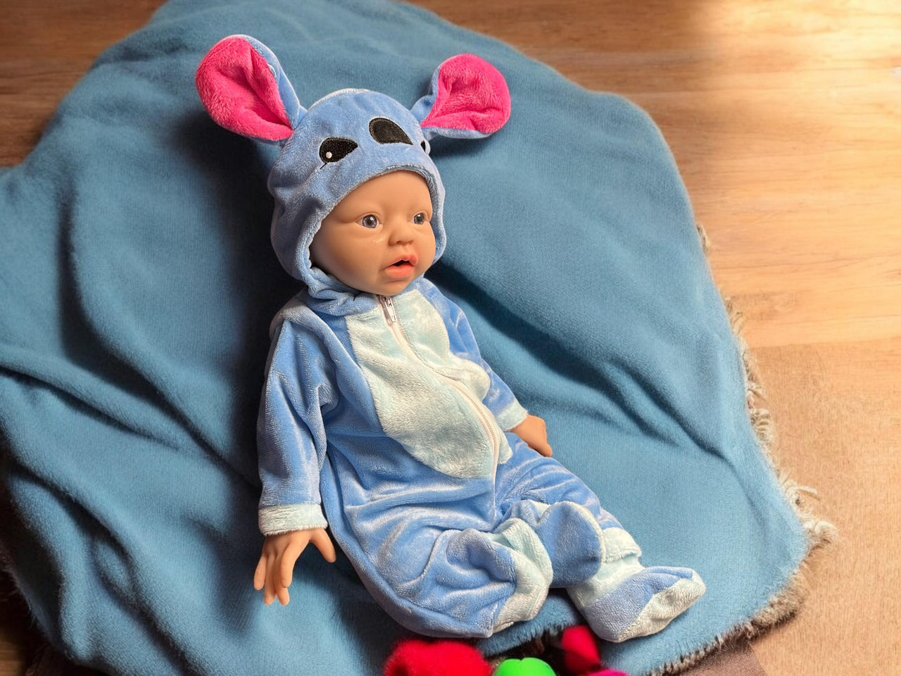 A baby doll wearing a blue outfit, featuring a cute expression and soft, plush material.