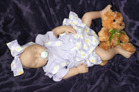Thumbnail for A baby doll wearing a purple dress, holding a teddy bear, sits on a soft surface, showcasing its charming features.