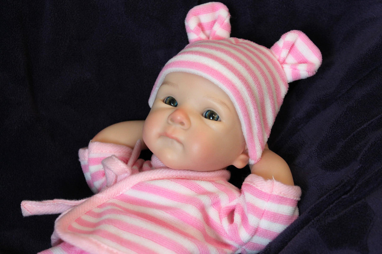 A baby doll wearing a pink and white striped outfit, showcasing a cute smile and round cheeks.