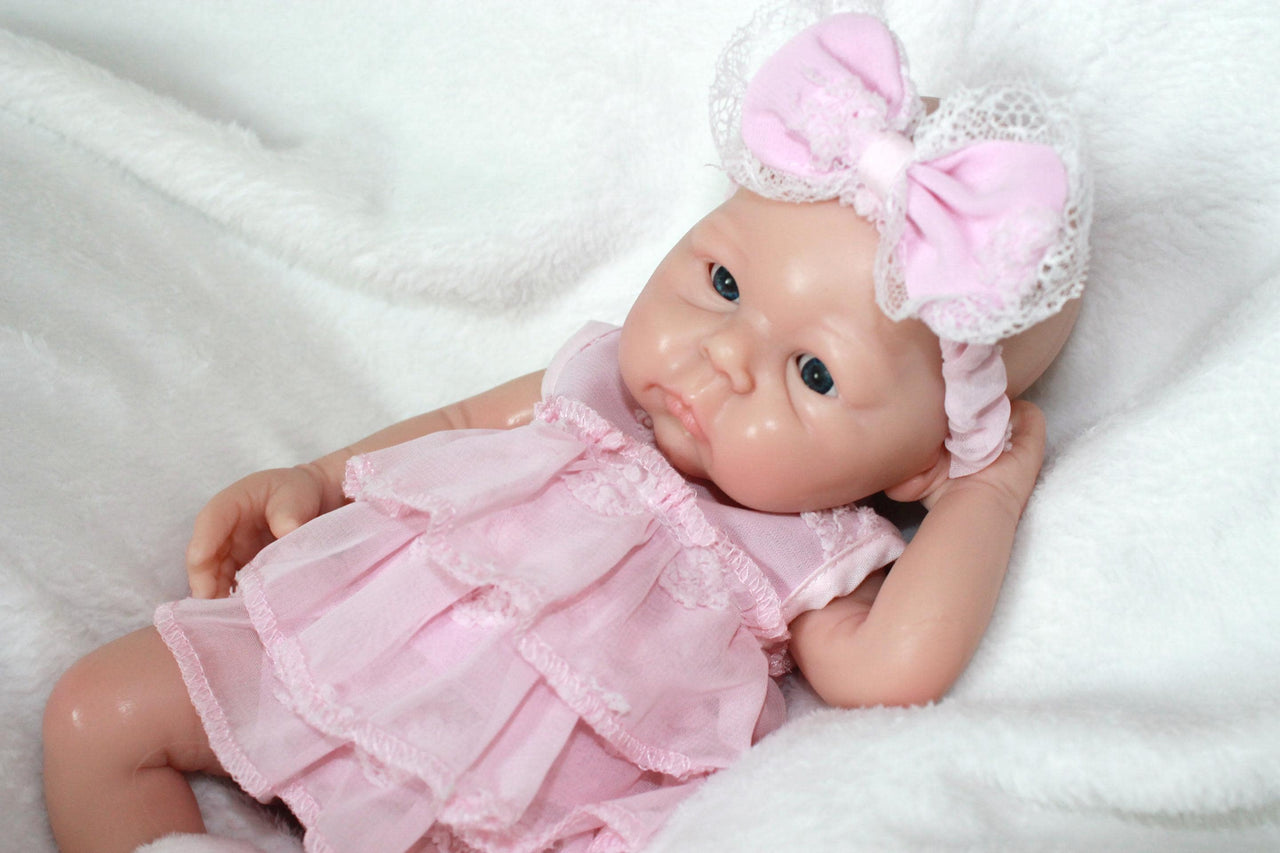 A baby doll adorned in a pink dress and headband, positioned on a light-colored surface.